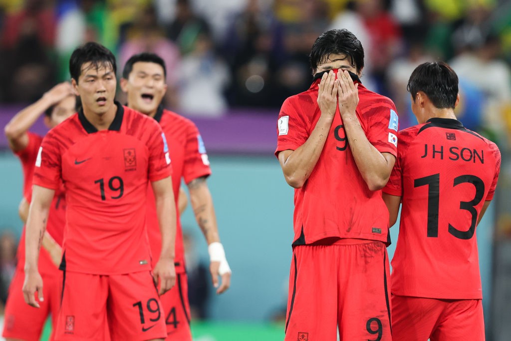 A South Korean player covers his face with his jersey during a Qatar World Cup match against Brazil. Teammates look tired around him.