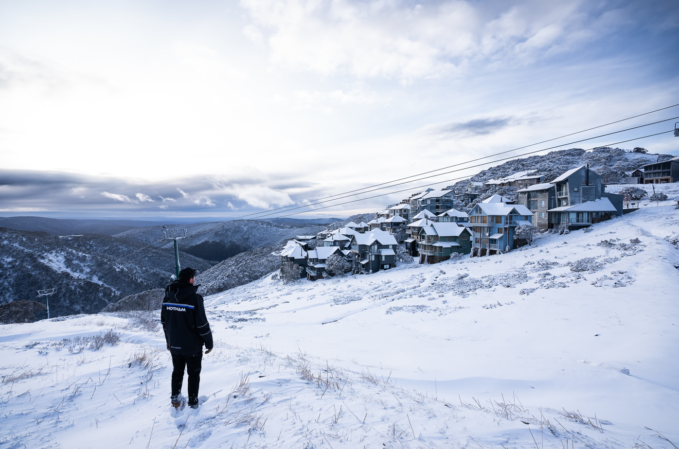 A man wearing a Hotham jackets standing in the middle of a snow covered field looking at Mt Hotham resort.