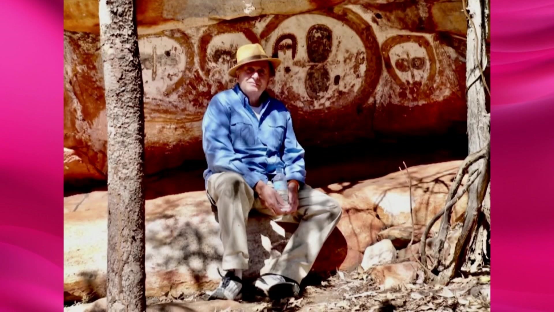 Barry Humphries sitting in front of rock art.