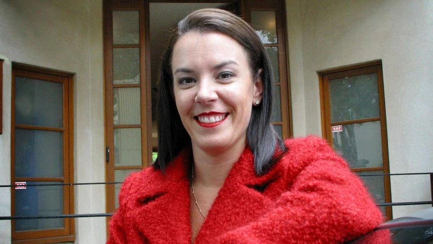 A middle-aged woman in a fluffy jacket smiles outside of a house