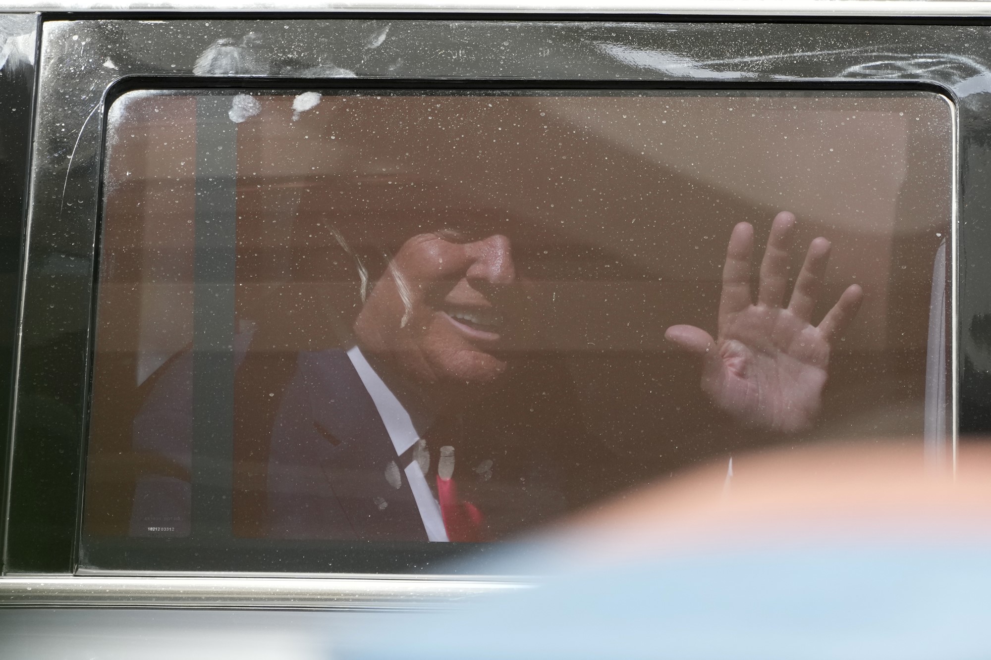 Donald Trump waving through the window of his car as he leaves the courthouse.