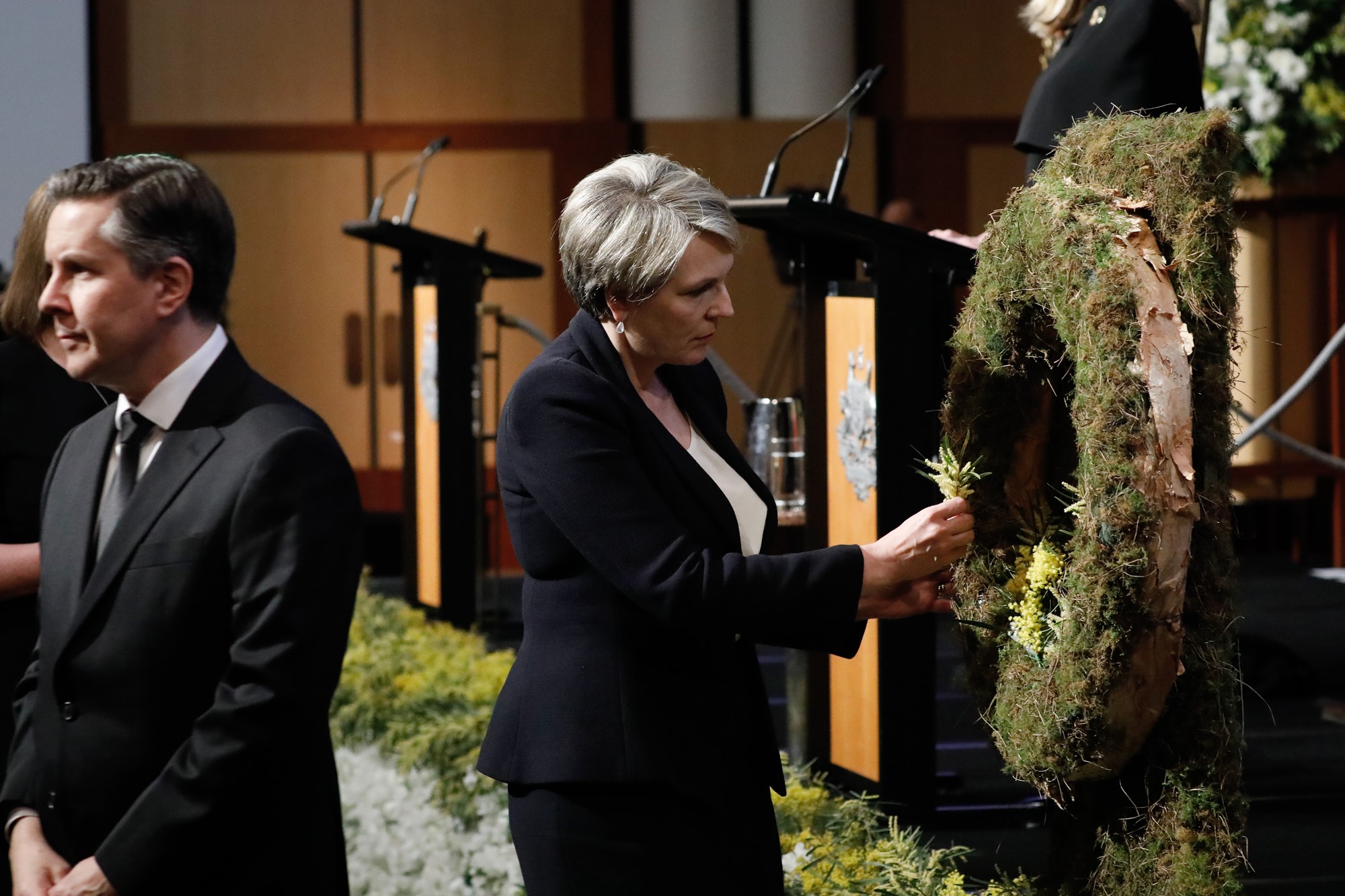 A woman places wattle on a wreath in the Great Hall.