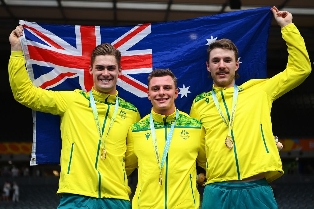 Three men hold an Australian flag up in the air