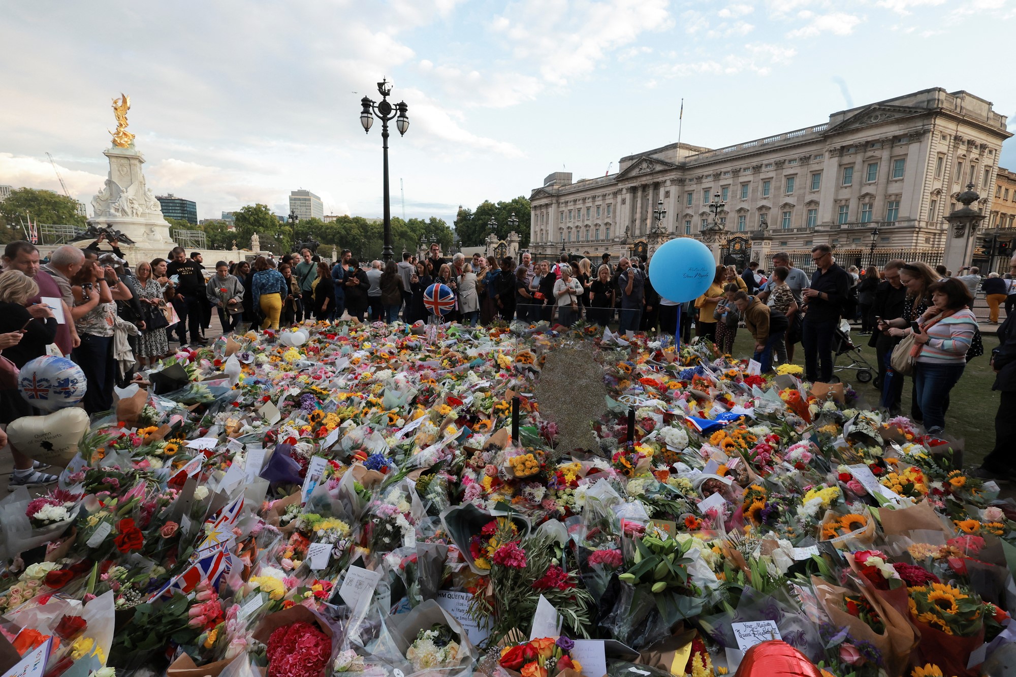 A sea of flowers and notes is pictured in front of Buckingham Palace, with people surrounding the floral tributes.