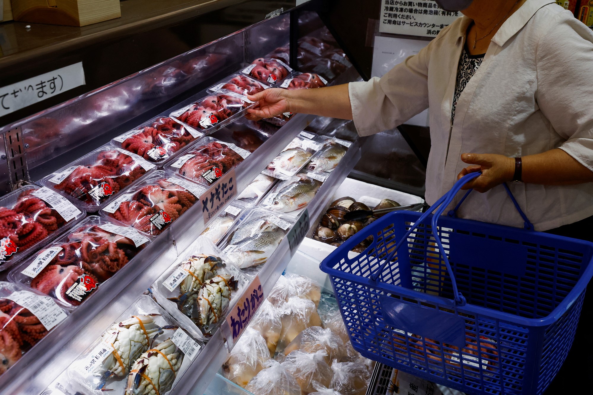 A woman reaches for a small tray of squid at a seafood counter.