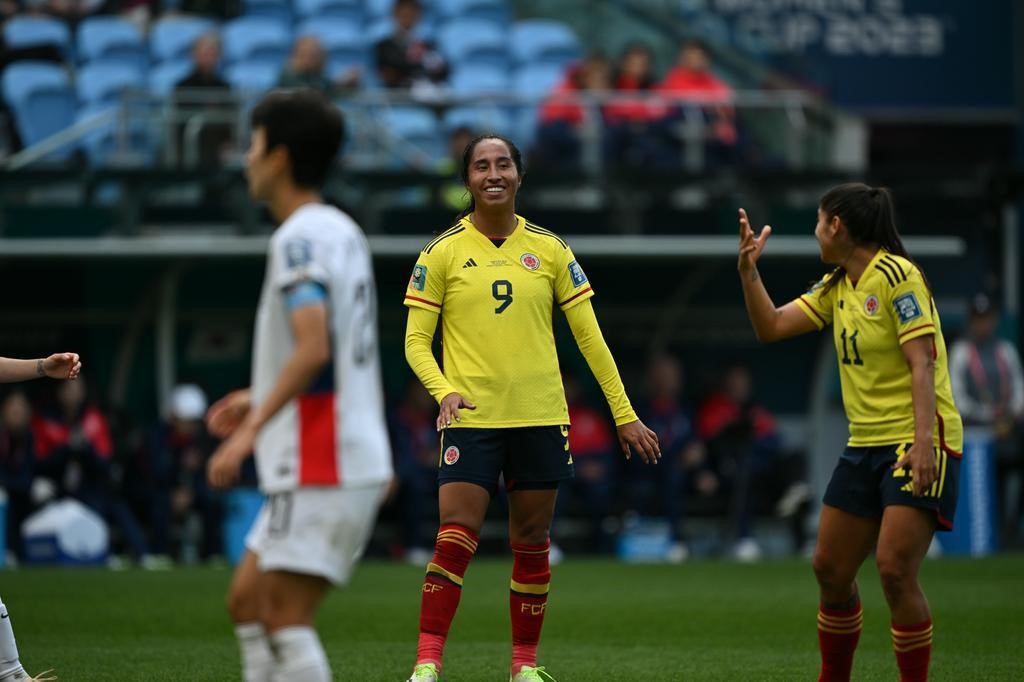 Colombia players smile while South Korean players talk in the foreground at the Women's World Cup.