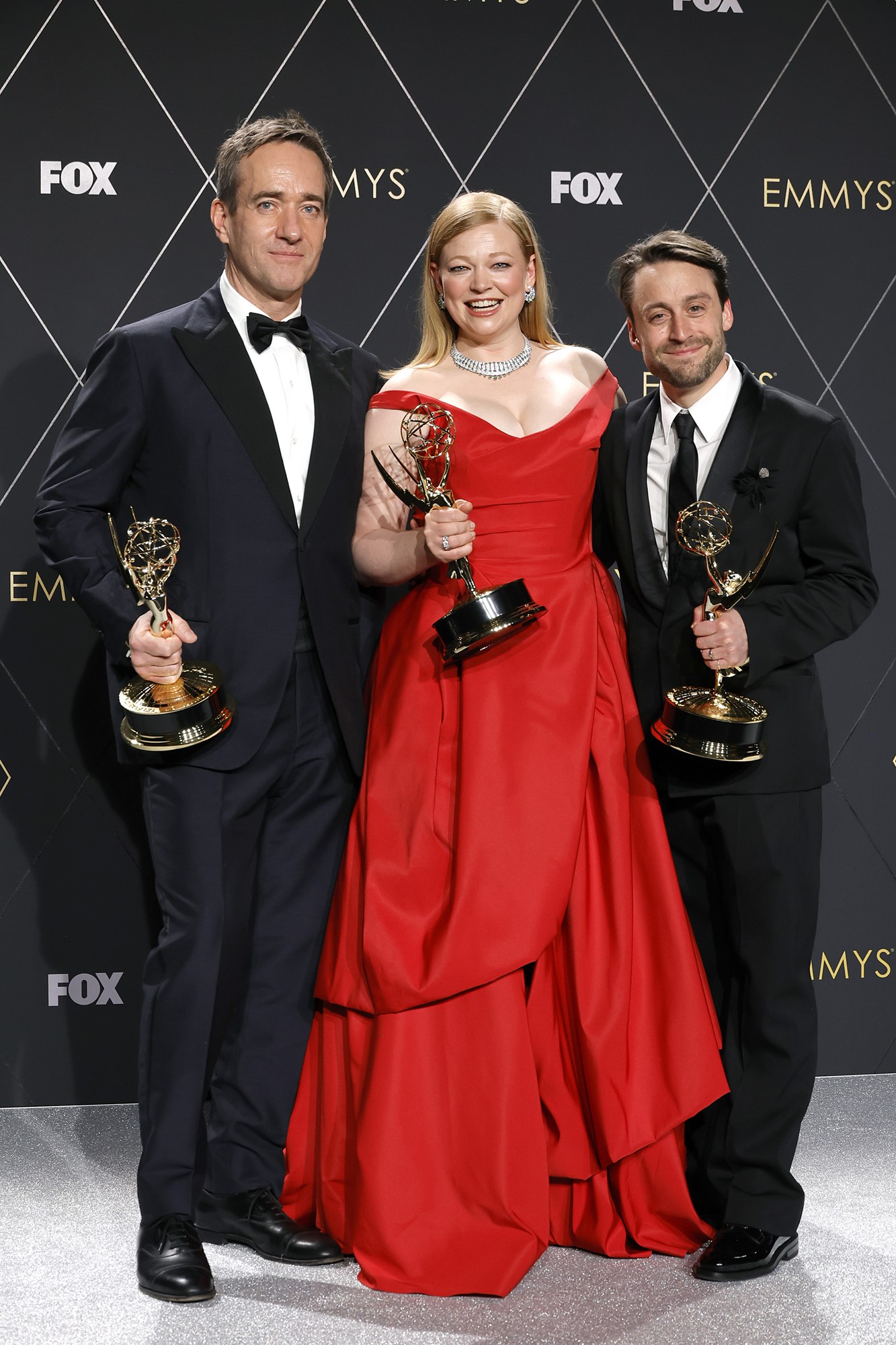 The three actors smile and hold up their gold Emmy statues.