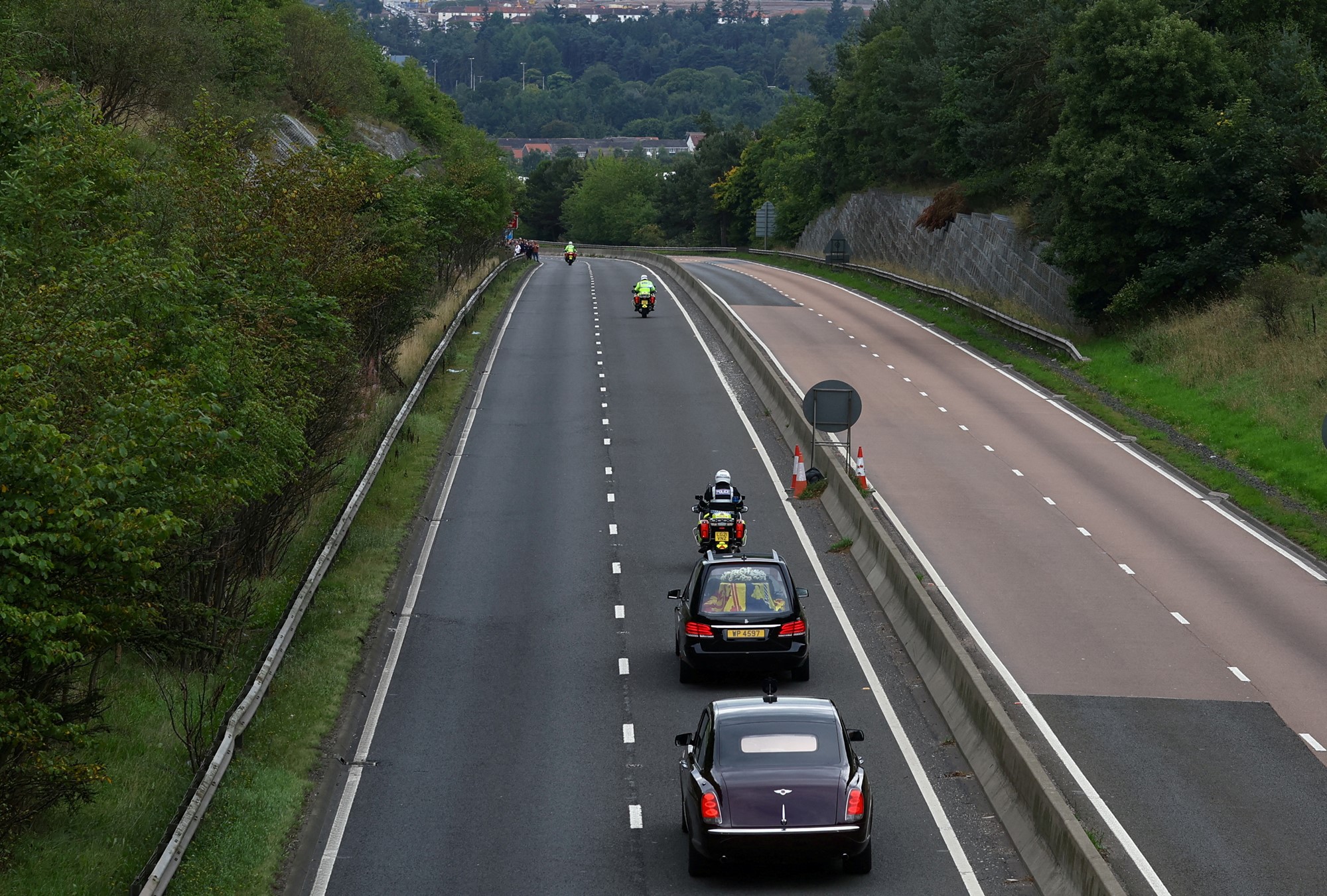 An empty highway is pictured with police on motorbikes, followed by a hearse and a black car.