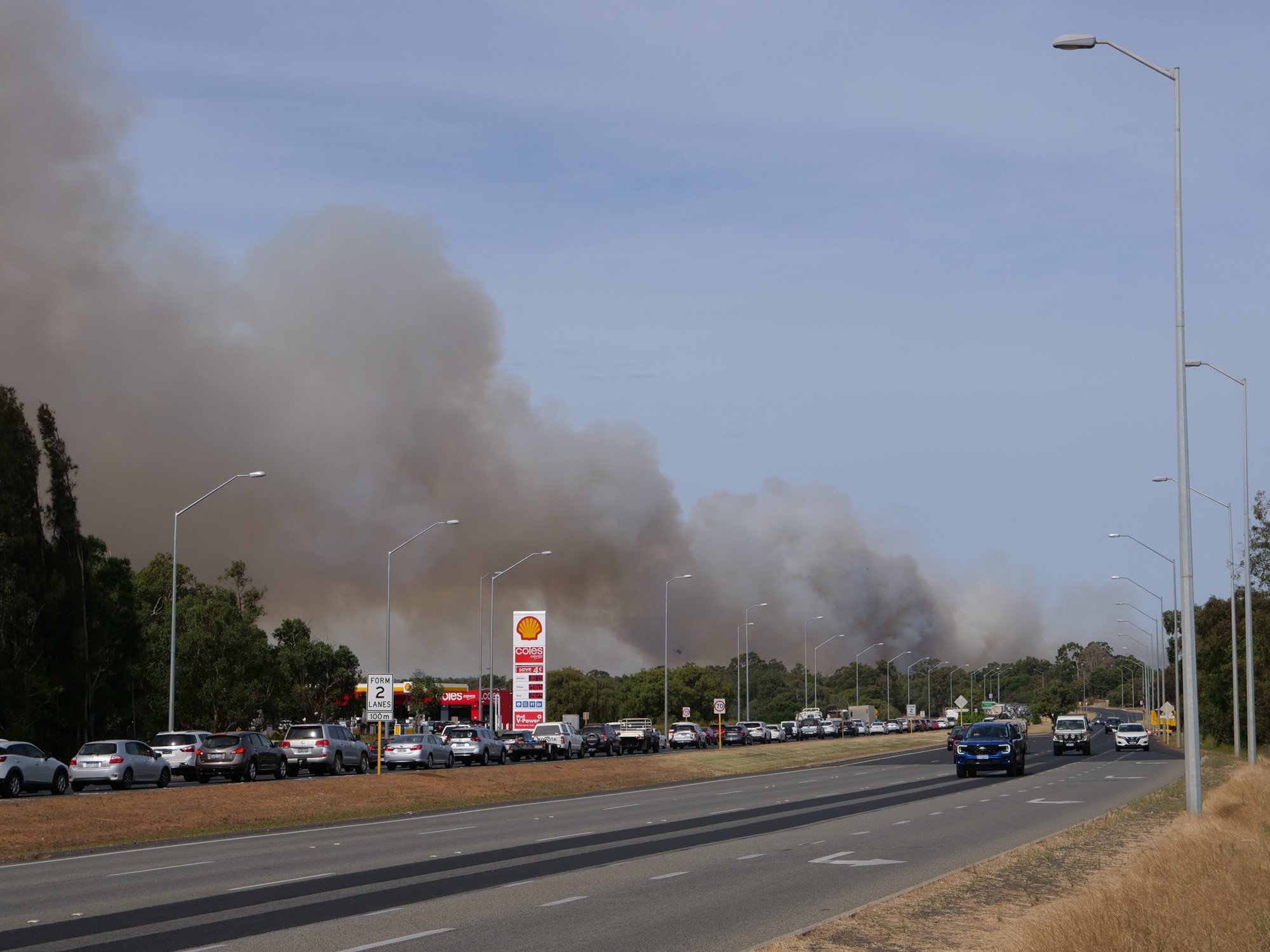 A highway with smoke in the background and a large line of cars backed up.