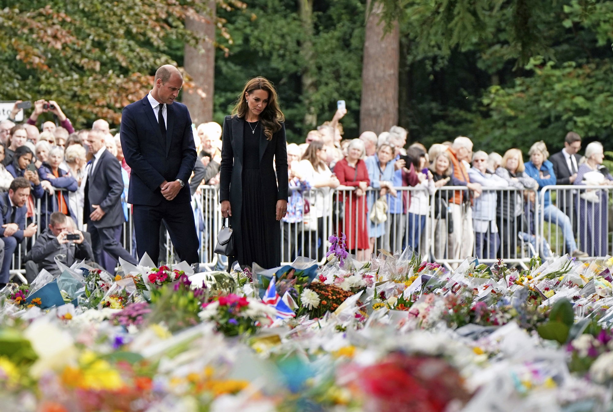 Prince William and Princess Kate look at bouquets of flowers in front of a crowd.