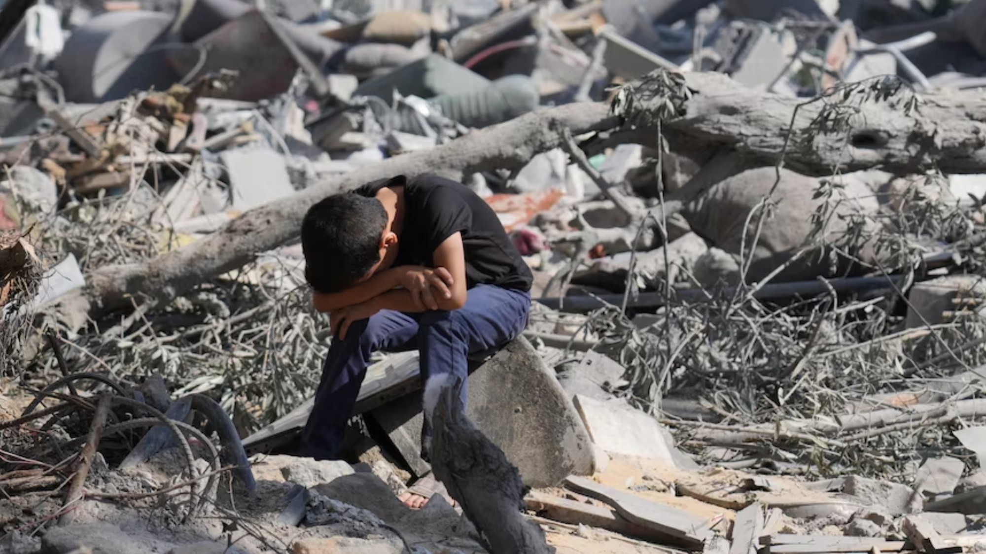 Ein Junge sitzt, den Kopf in den Händen, auf einem Stück Beton, umgeben von Trümmern
