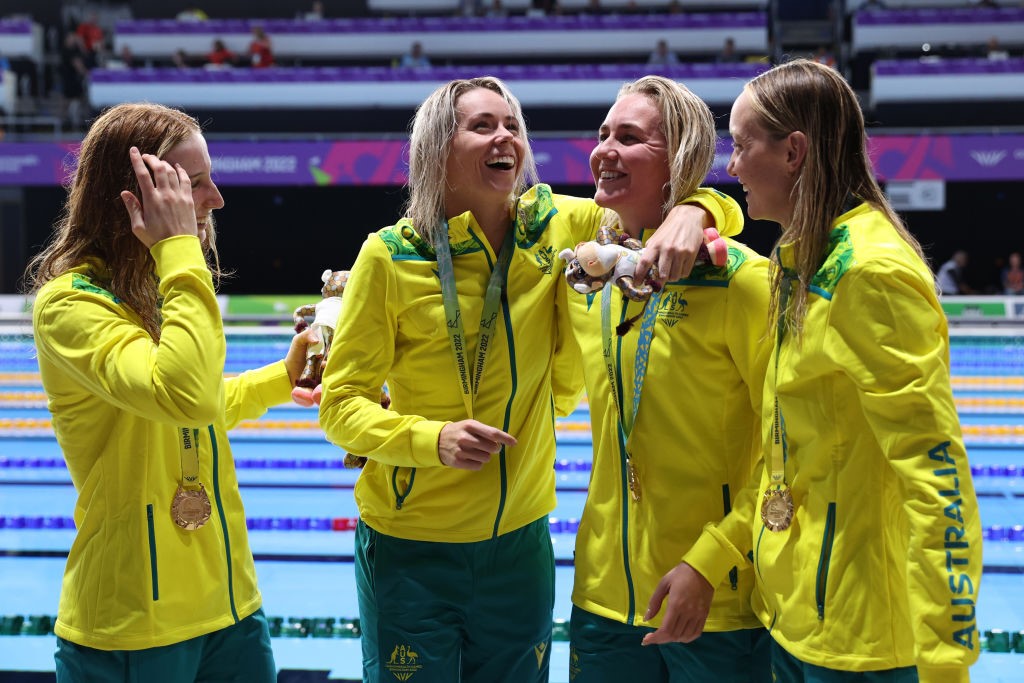 Madison Wilson, Kiah Melverton, Ariarne Titmus and Mollie O'Callaghan smile and laugh with gold medals around their necks in front of a pool