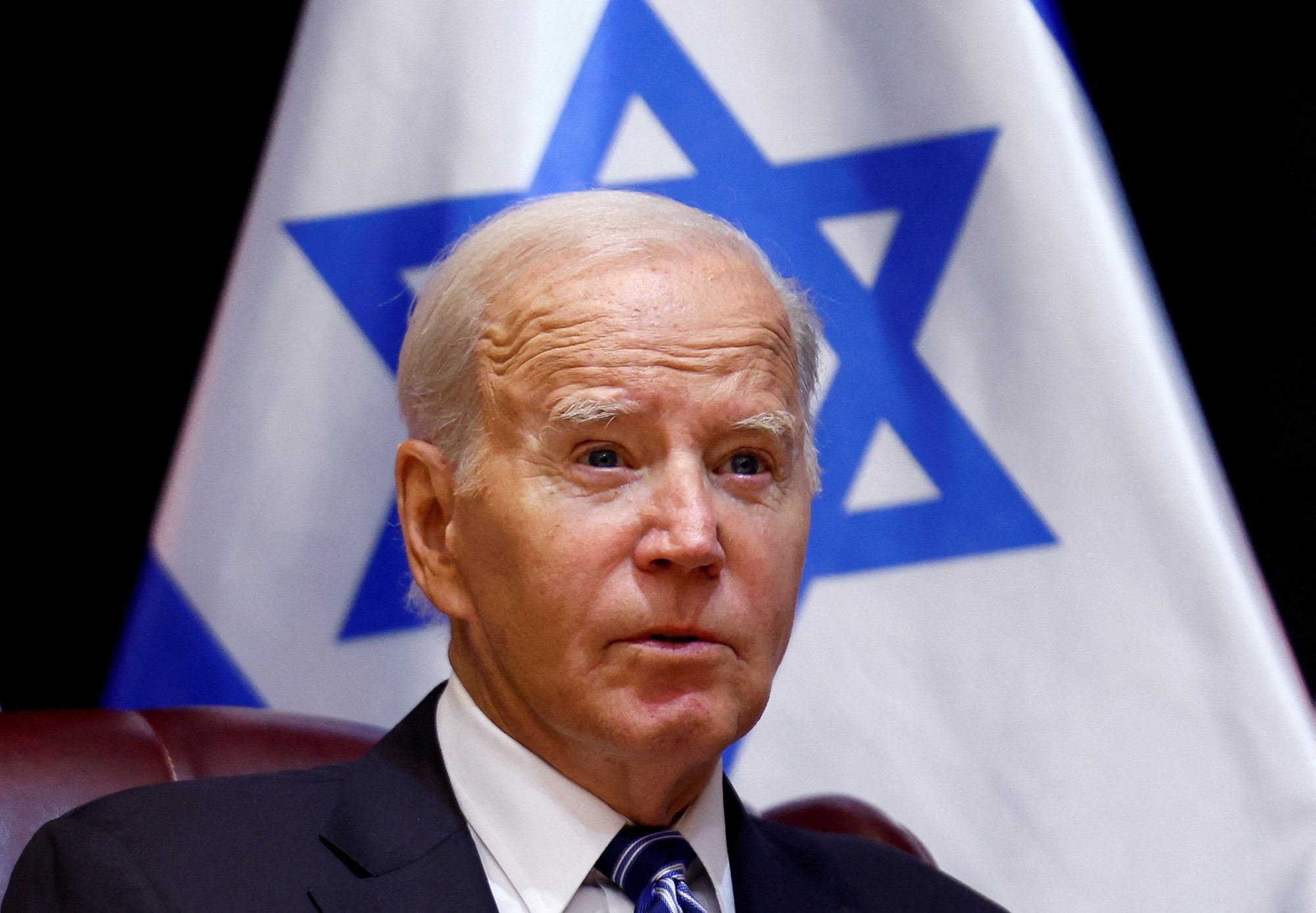 Portrait photo of US President Joe Biden sitting in front of an Israeli flag.