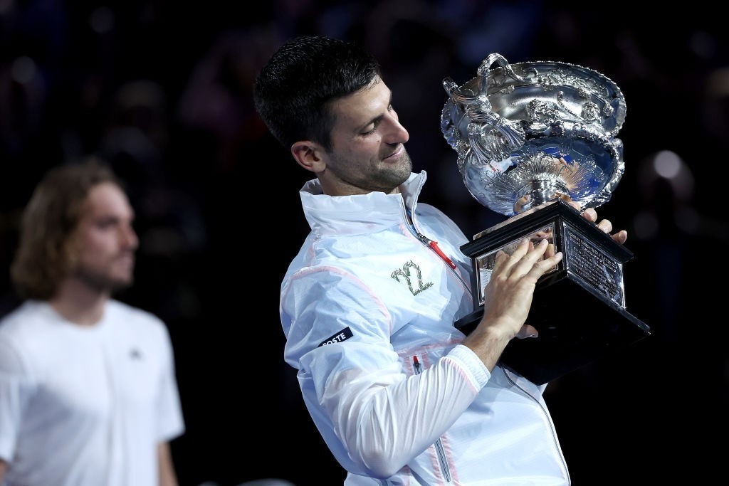 A man wearing a white jacket holds a silver trophy.