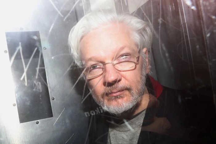 Julian Assange, wearing glasses, sits in prison van