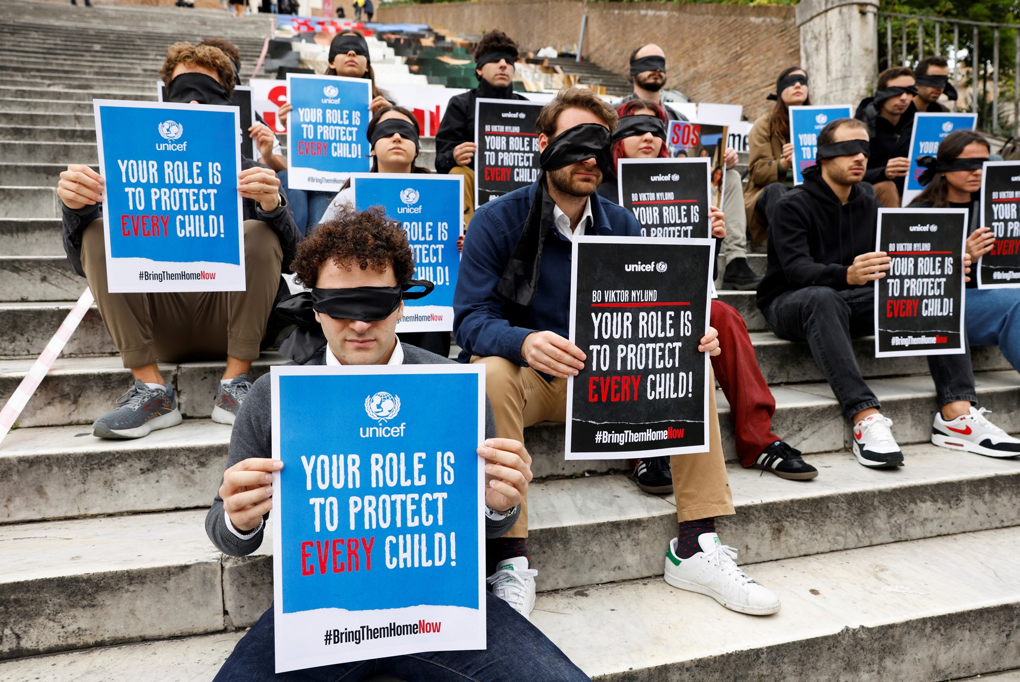 A gorup of people hold signs while blindfolded on steps 