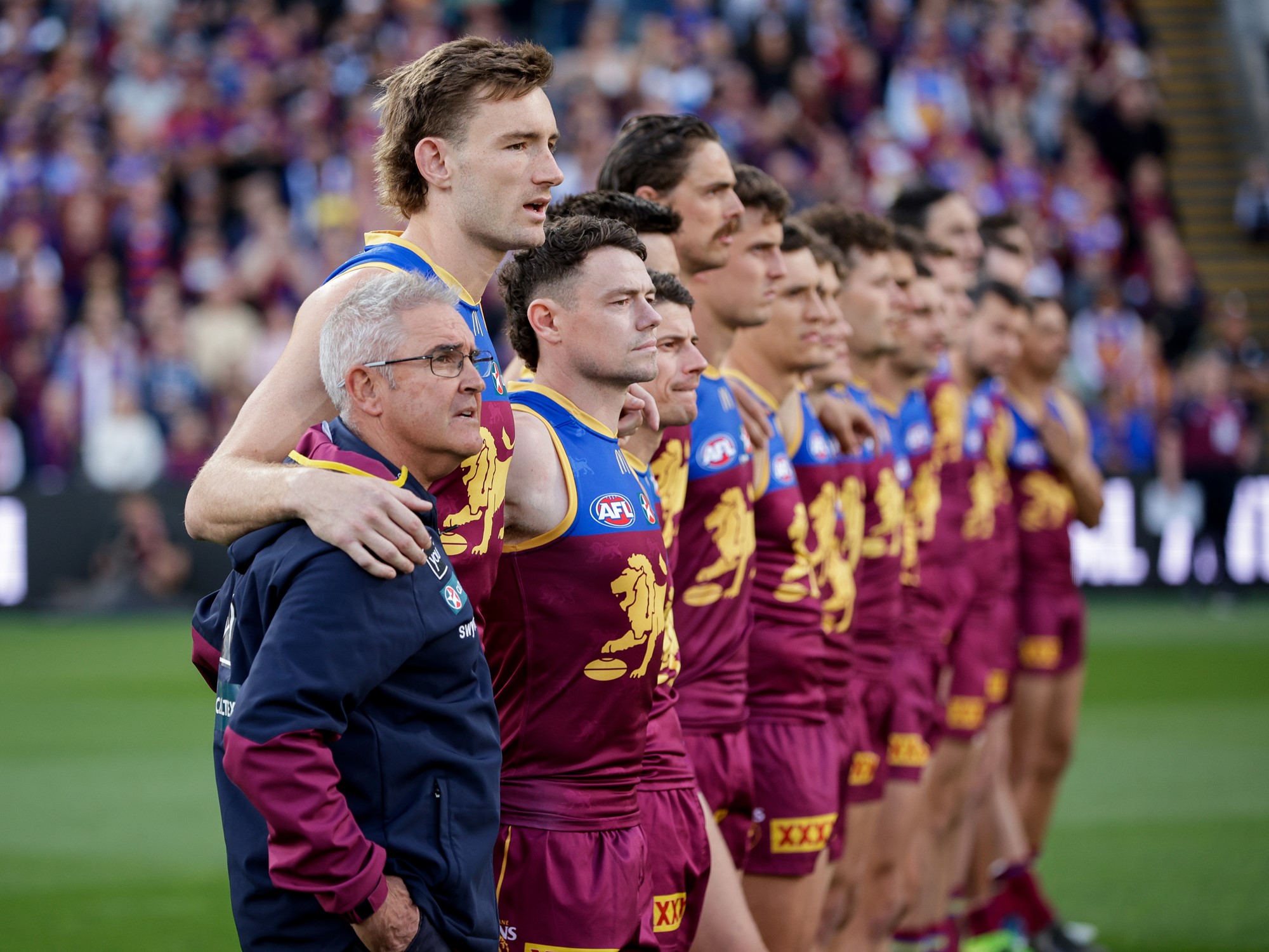 The Brisbane Lions stand arm in arm as they sing the national anthem.