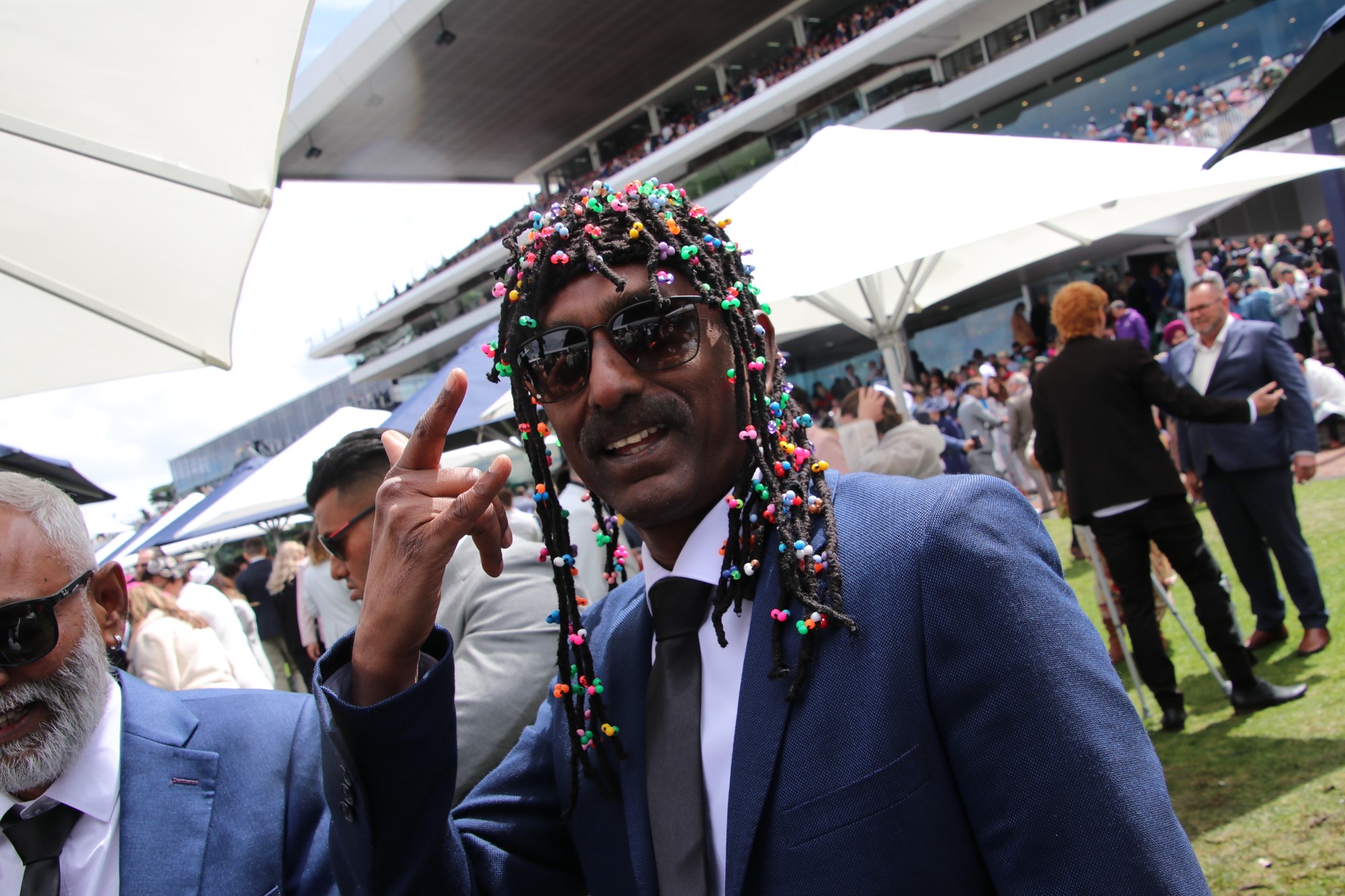 A man with colourful dress waves, standing outside.