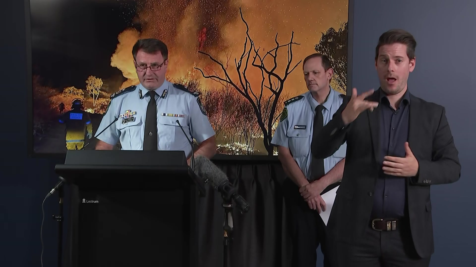 A man in a police uniform speaks at a lectern.