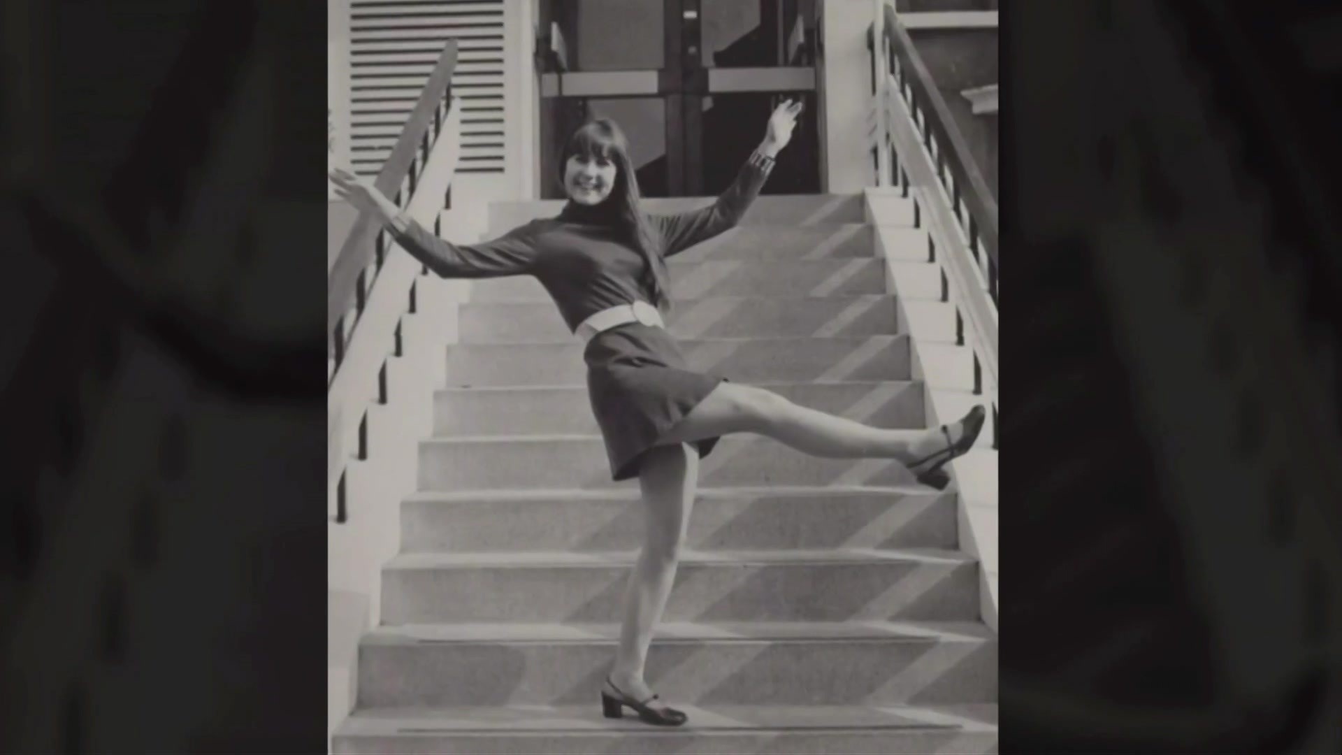 Judith Durham smiles and stands on some stairs.