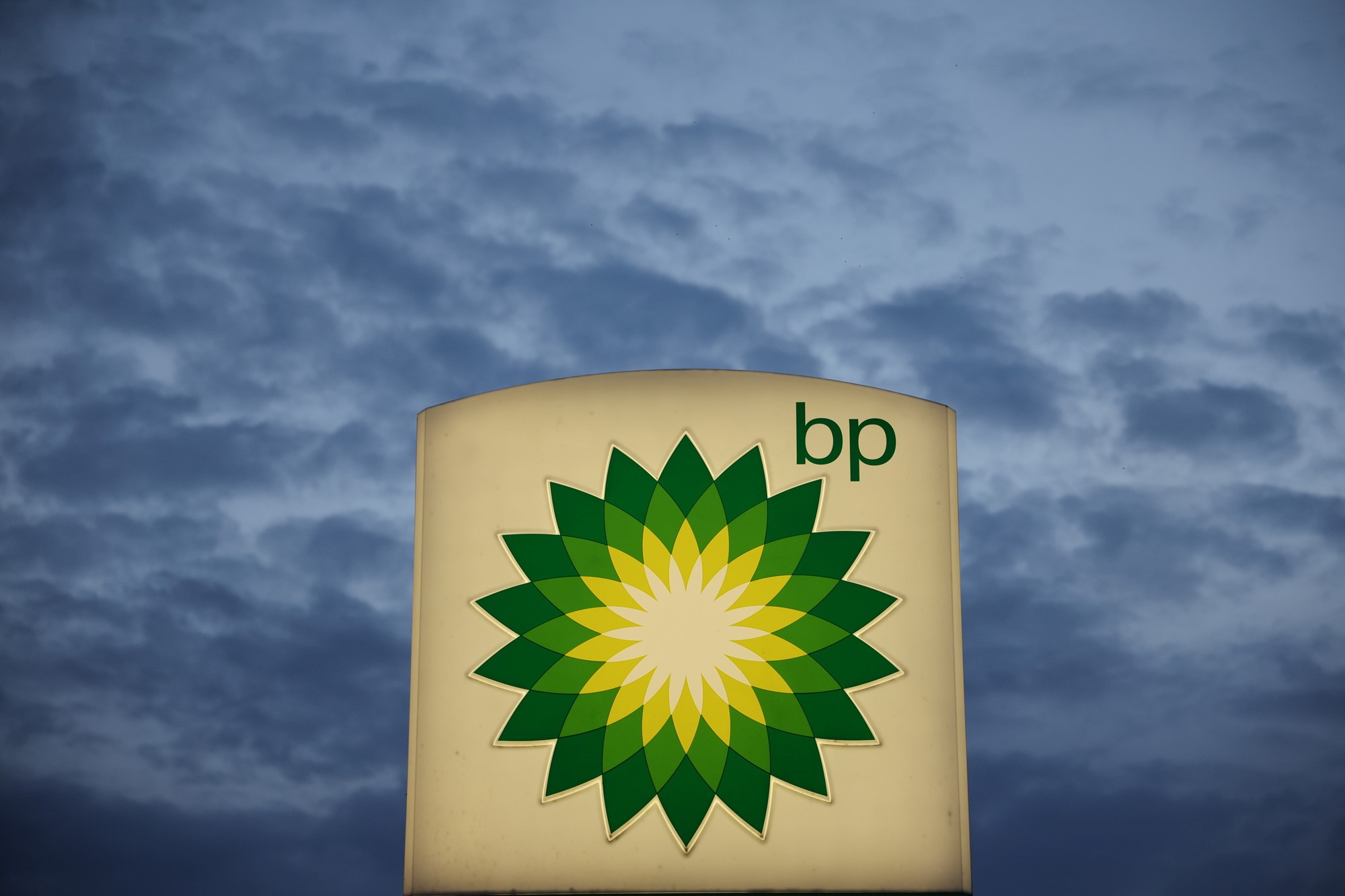 A sign with BP's logo with a dark sky and clouds behind it.
