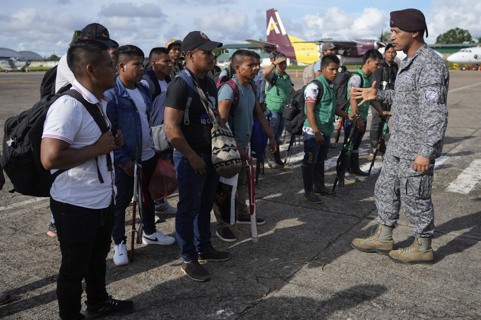 A group of men with bags speaking to a man in military uniform on the tarmac of an airport