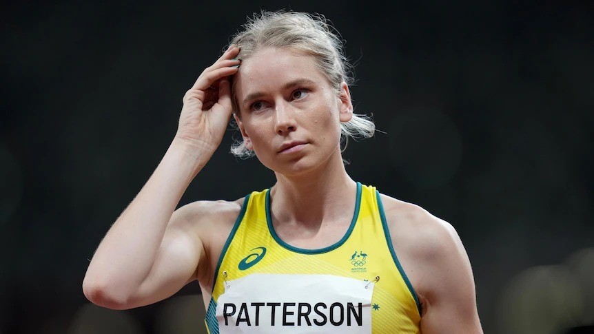 Eleanor Patterson, wearing green and gold athletics gear, tucks her hair behind her ear.