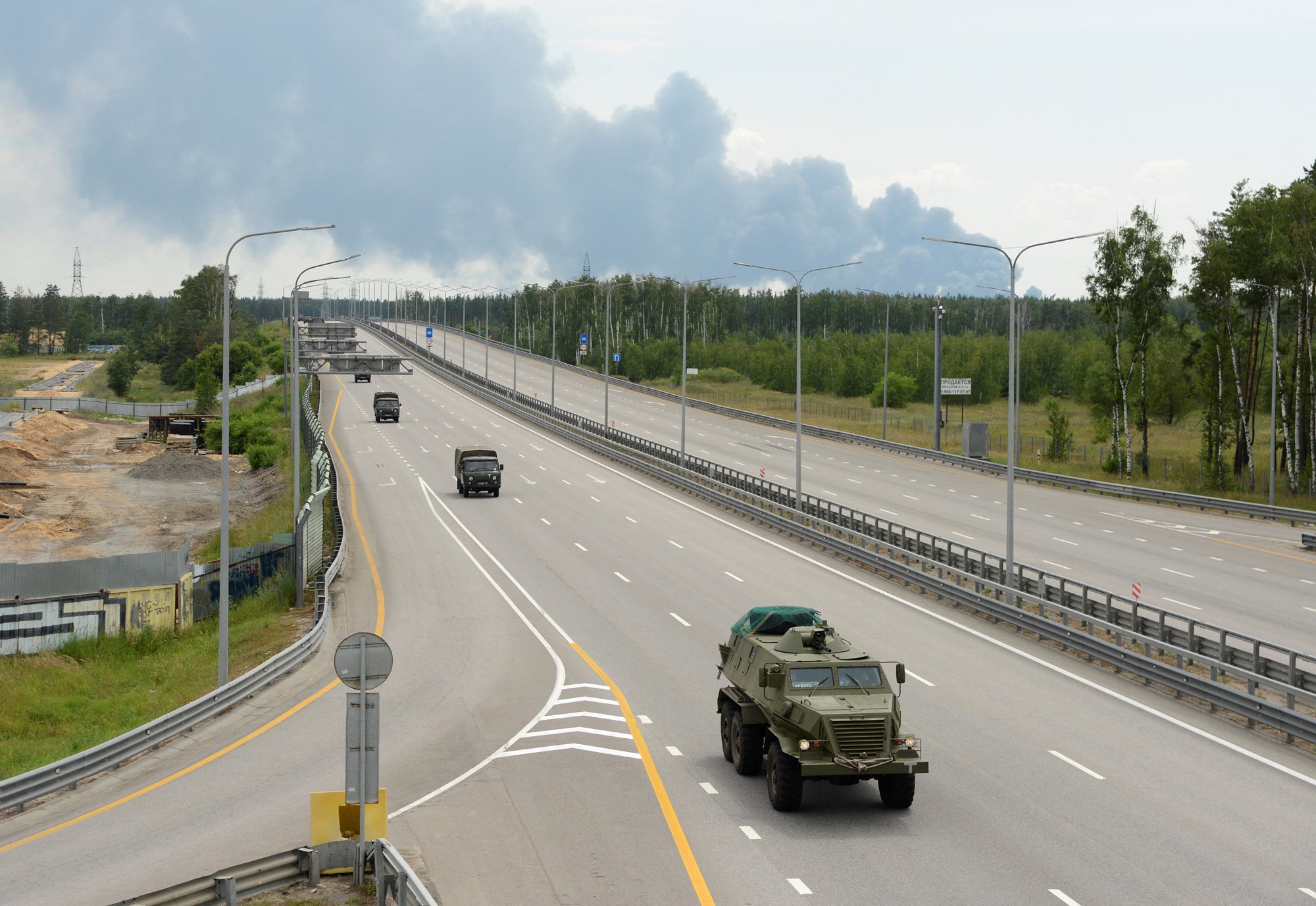 Four military vehicles drive along an empty highway