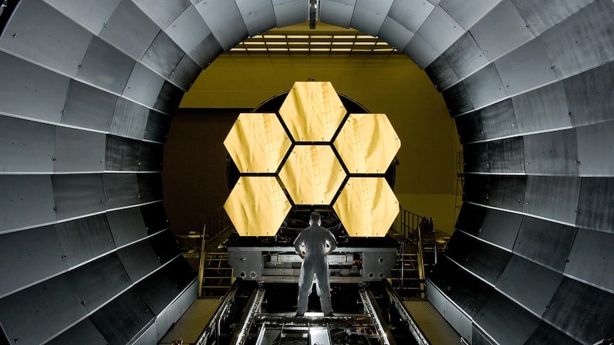 An astronaut stands in front of the telescope.