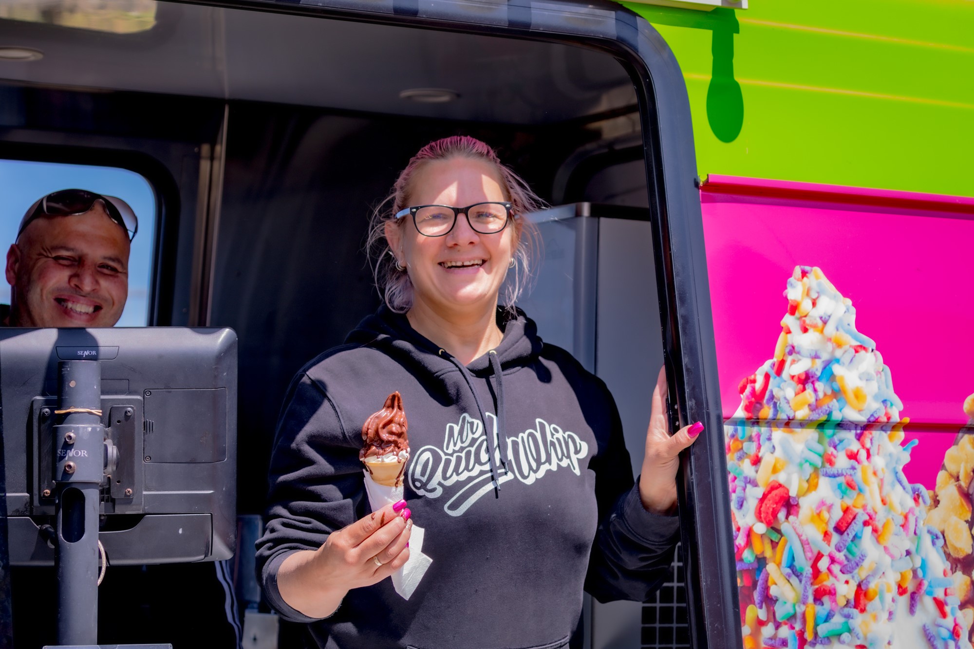 A woman in an ince-cream truck holding a soft serve ice cream