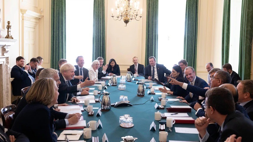 Boris Johnson stands in the middle of the room while his staff stand around him, some applaus while others smile.