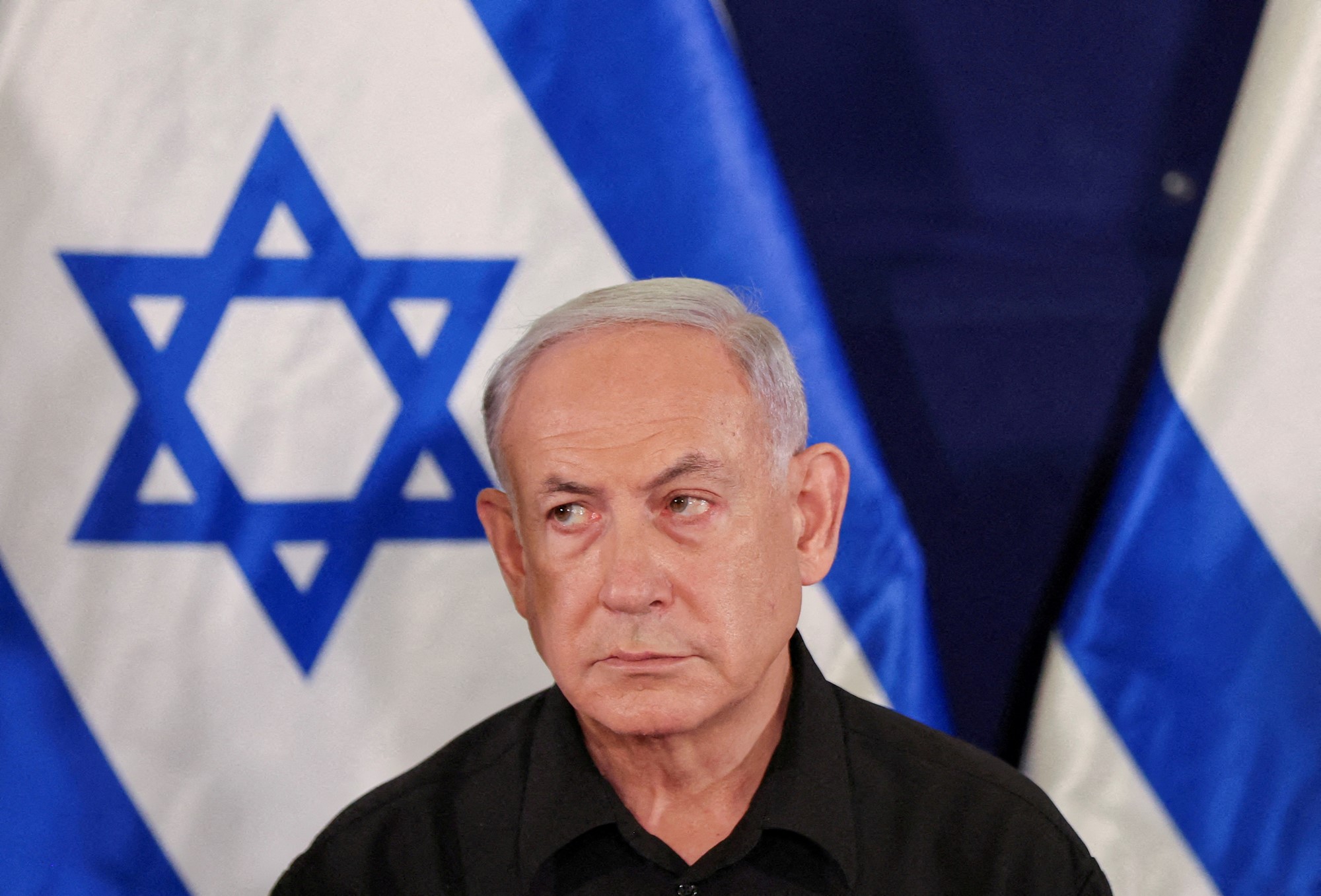 Benjamin Netanyahu looks sternly in front of Israeli flag. 