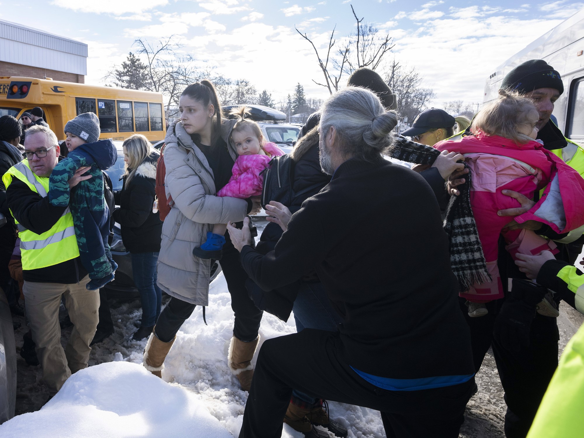 Parents and their children are loaded onto a warming bus as they wait for news after a bus crashed into a daycare centre in Laval, Quebec, on Wednesday, Feb. 8, 2023.