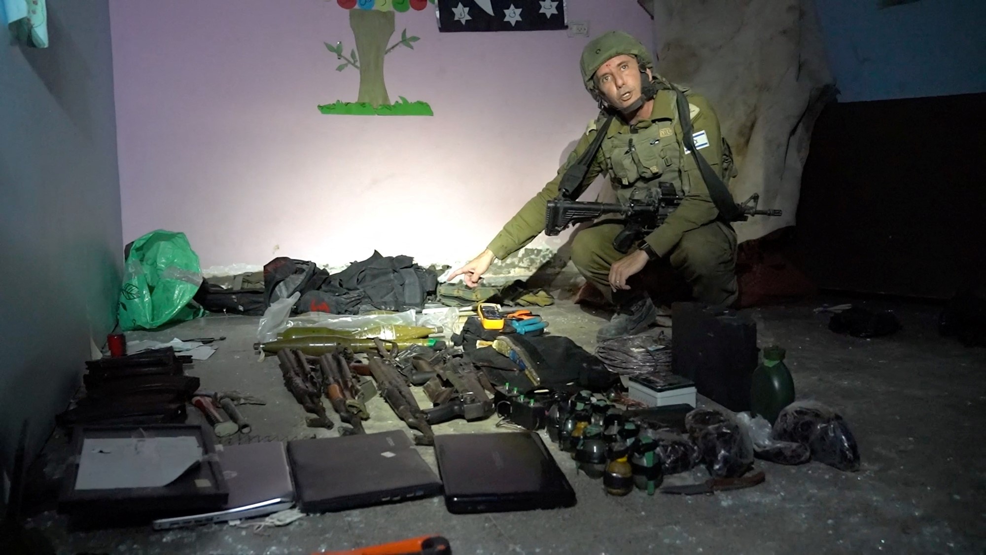 A man wearing a military uniform squatting near weapons laid out on the floor