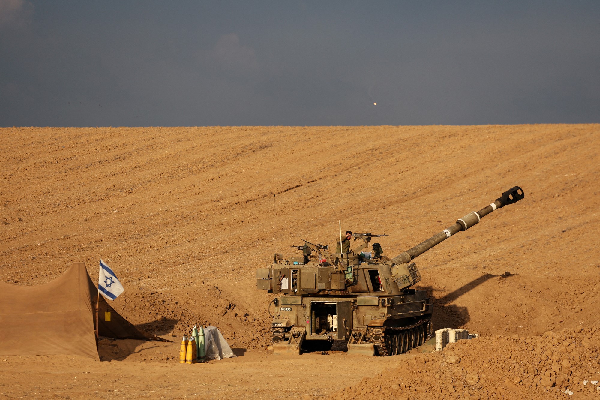 An Israeli soldier shades his eyes from the sun as he stands on a self-propelled howitzer
