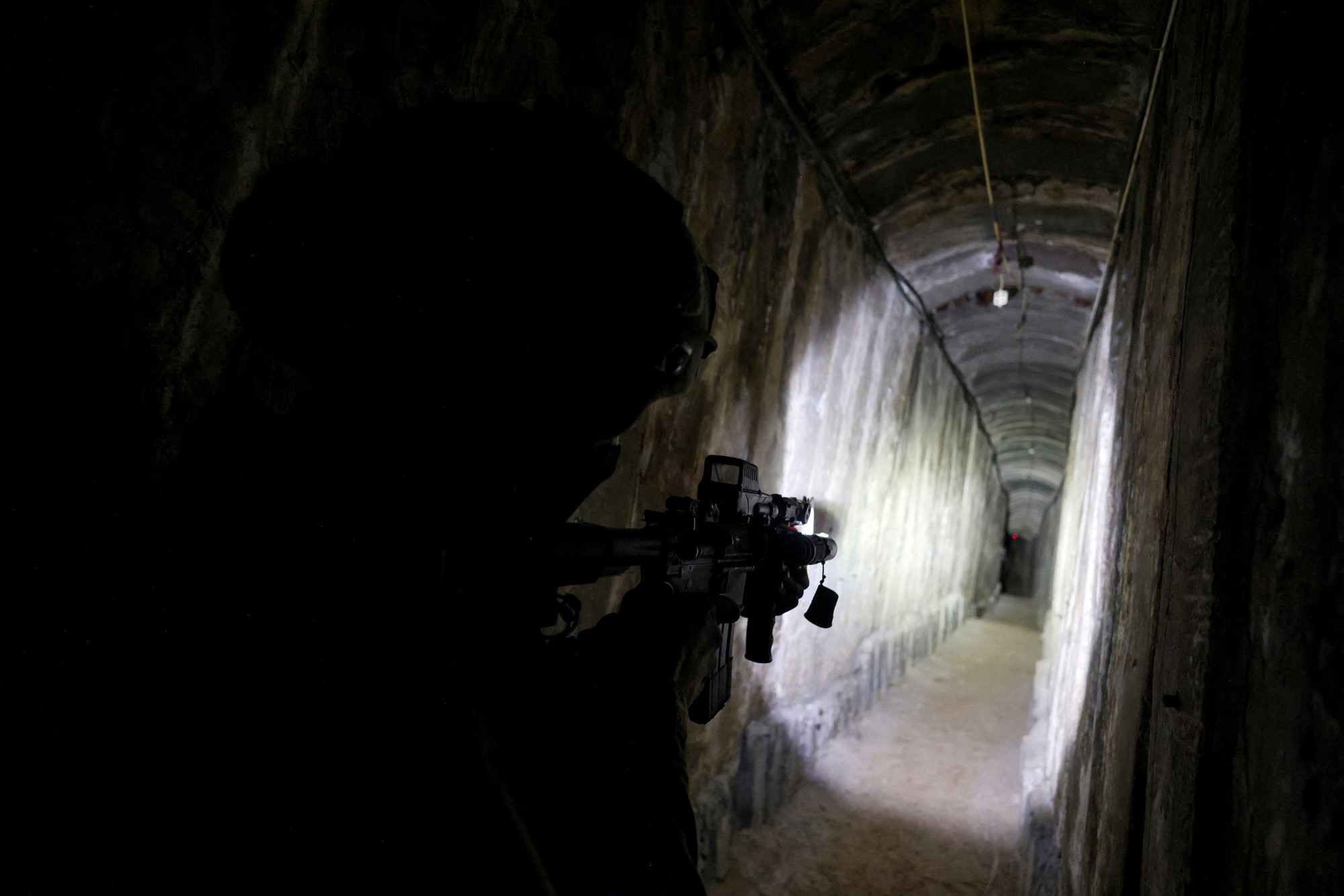 The silhouette of a soldier with a gun is pictured as a flashlight shines through a tunnel.