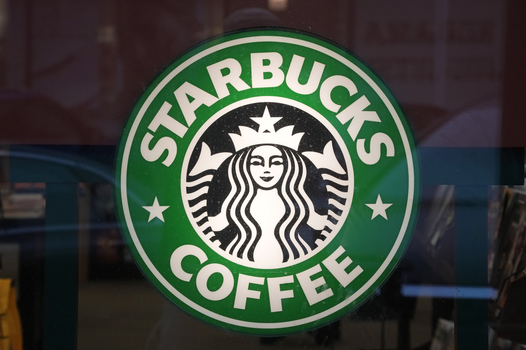 The starbucks logo which has a mermaid inside a green circle with the words starbucks coffee written on it,  on a glass window.