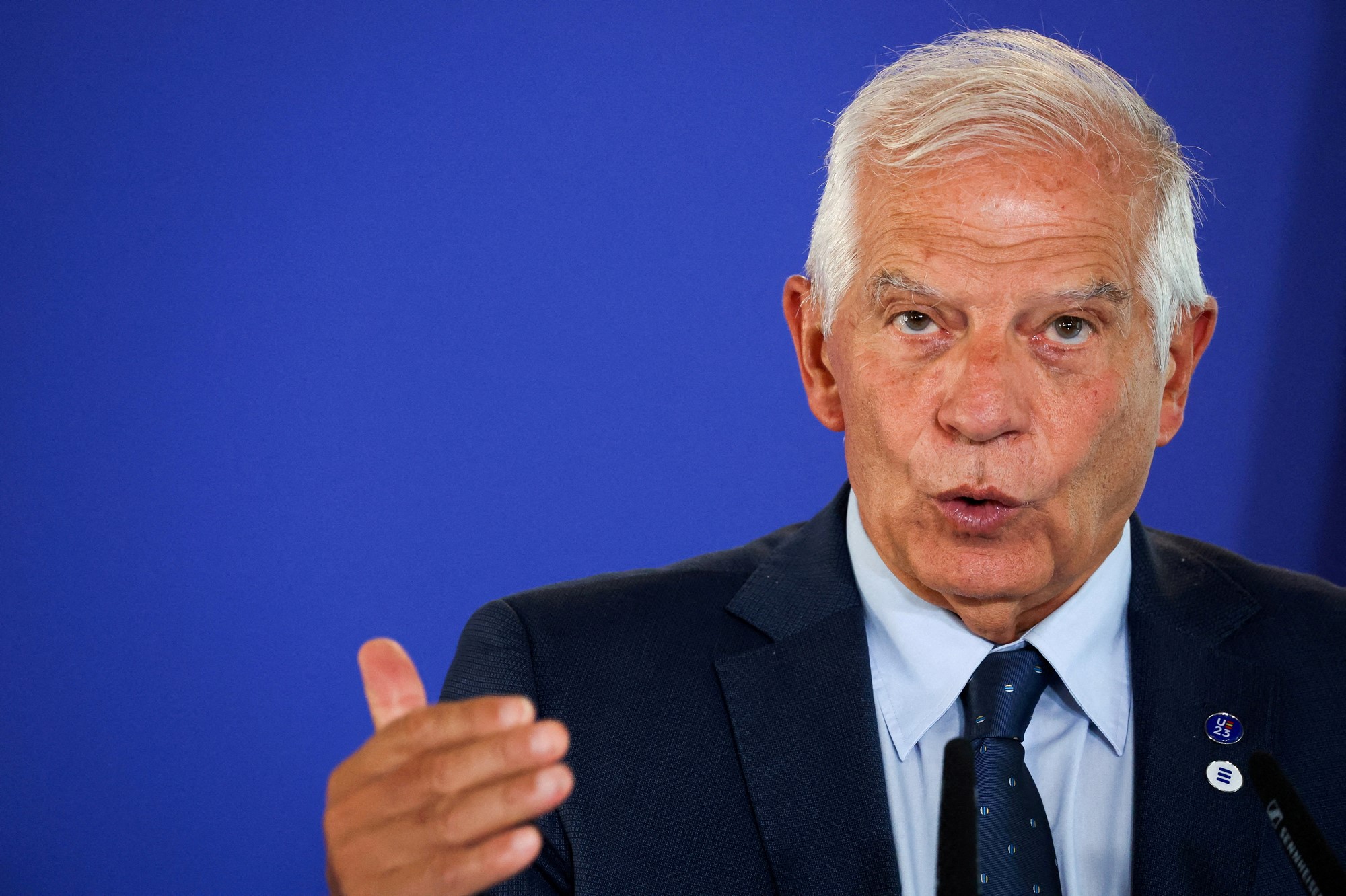 Man with white hair wearing suit gestures with his hand. 