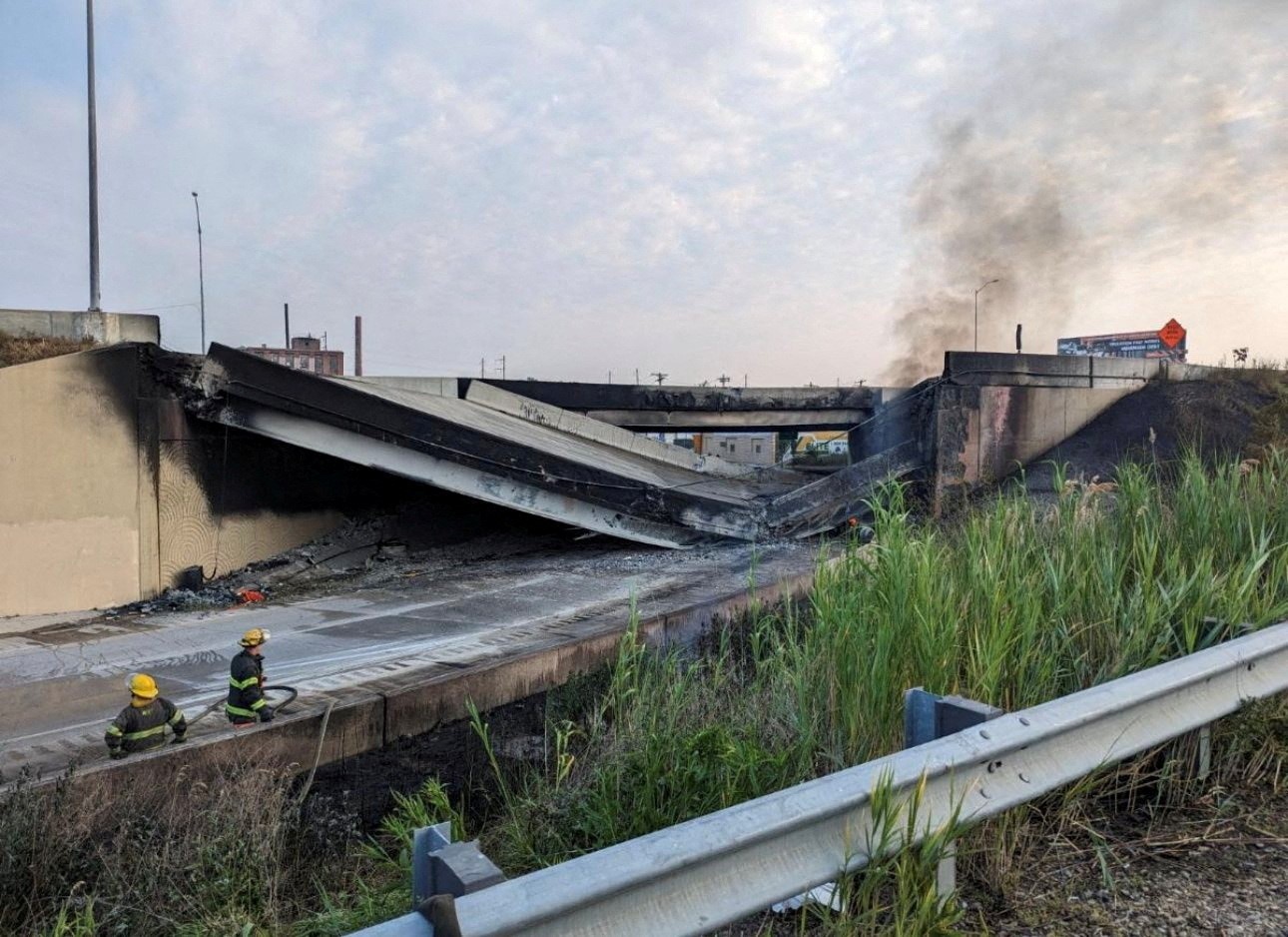 Fire crews work in front of the smouldering rubble of a collapsed highway overpass