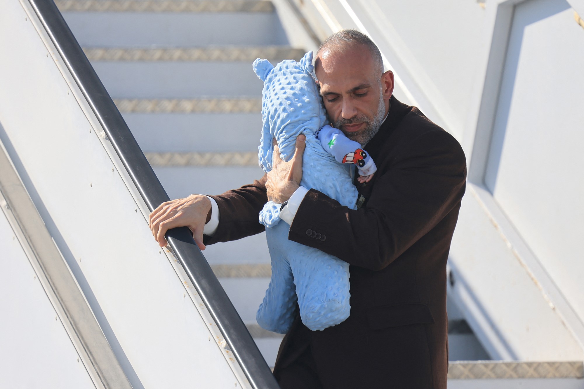 A man holding a small child on the stairs of a plane. 