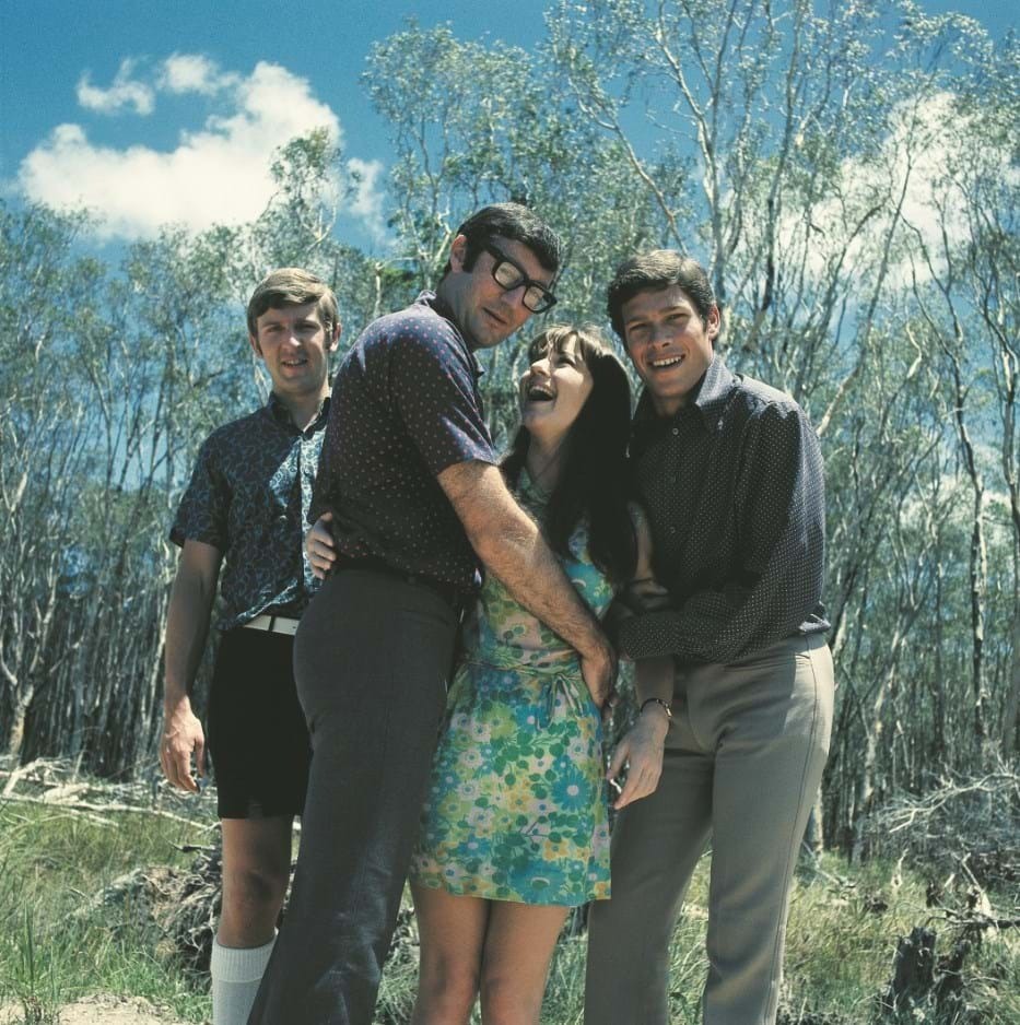 The members of The Seekers smile and hold each other in bushland.