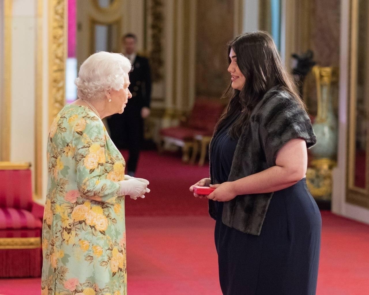 The Queen presents an award to a woman in a black dress.