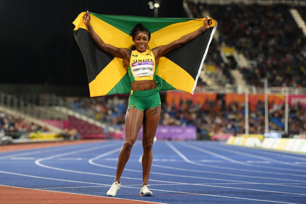 A woman stands holding a Jamaica flag behind her