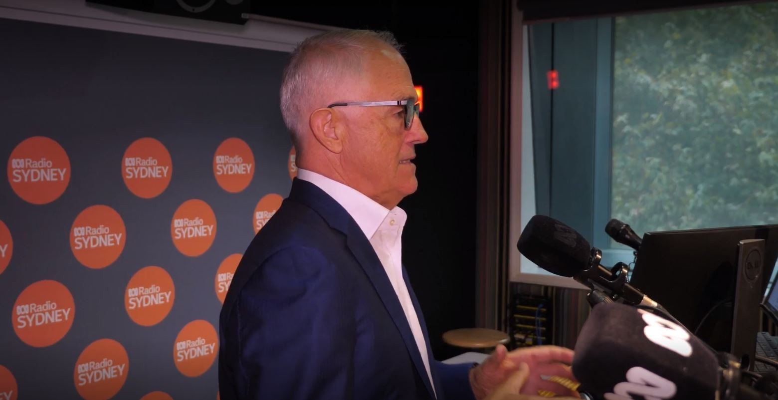 Man with glasses stands in radio studio at microphone