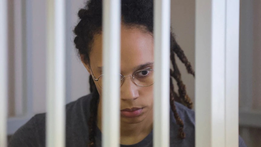 Brittney Griner stares blankly towards the ground, behind white courtroom bars