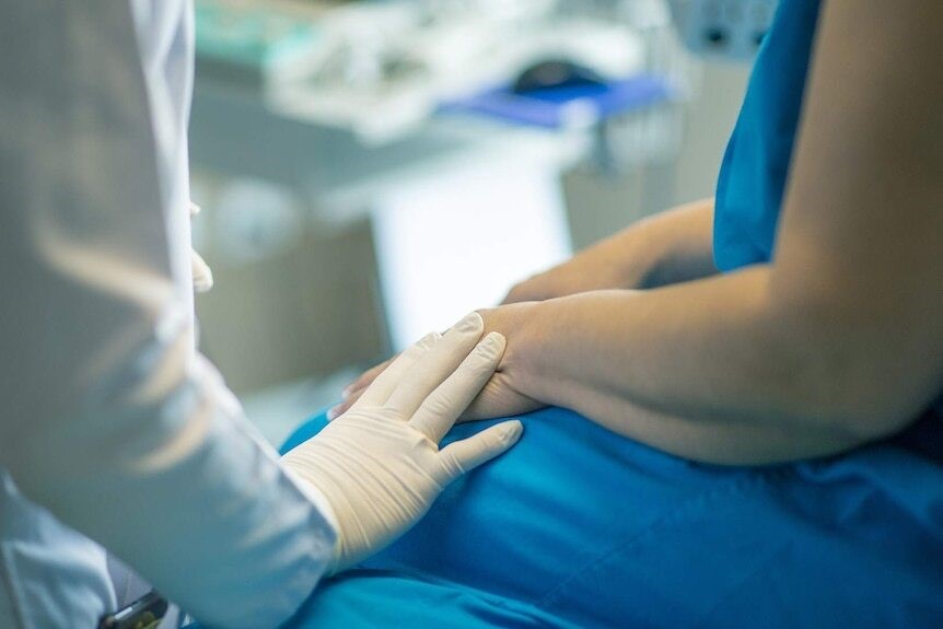 A close up of a doctor placing their hand on a patient's hand out of concern.