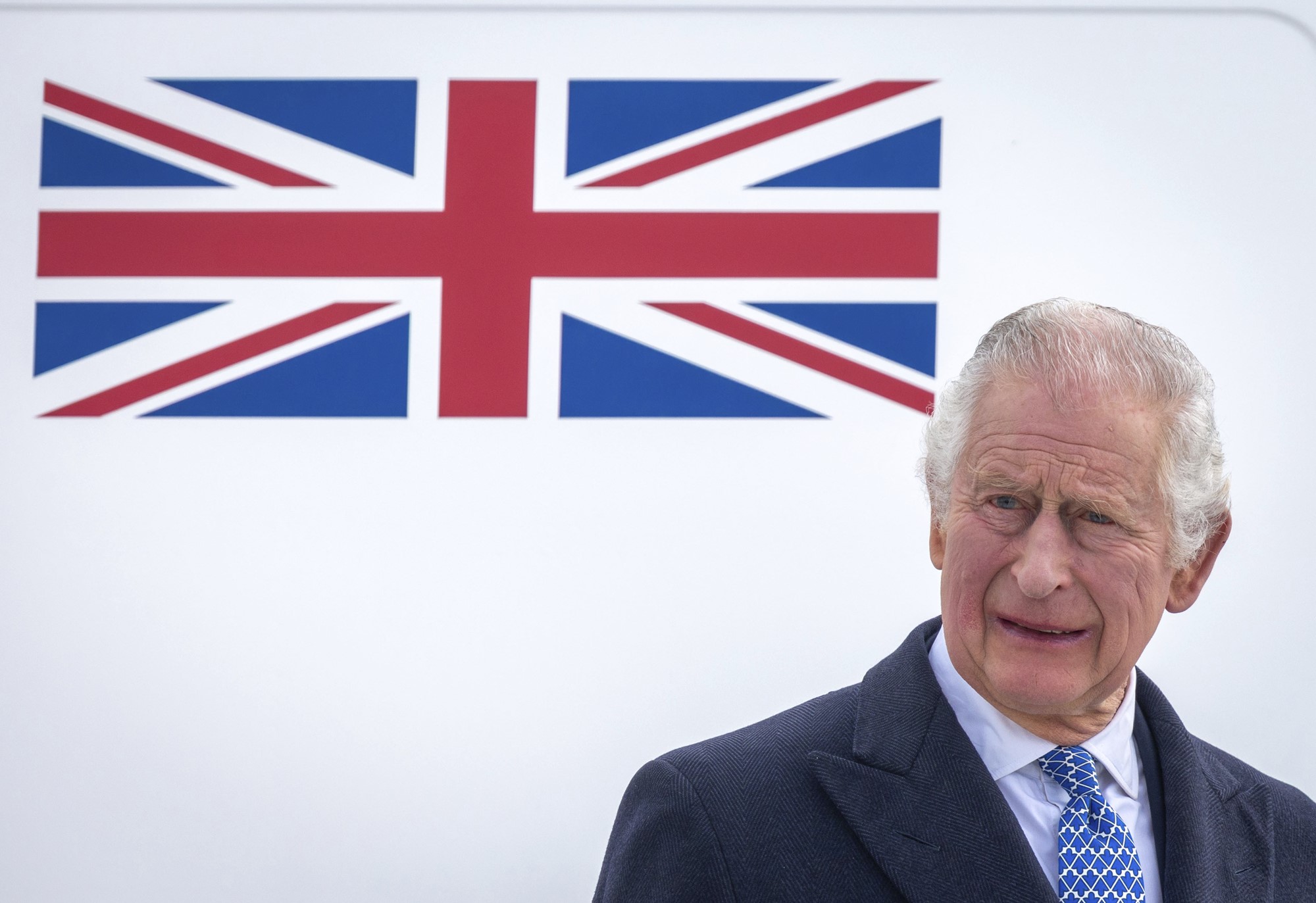 King Charles III stands in front of the Union Jack.
