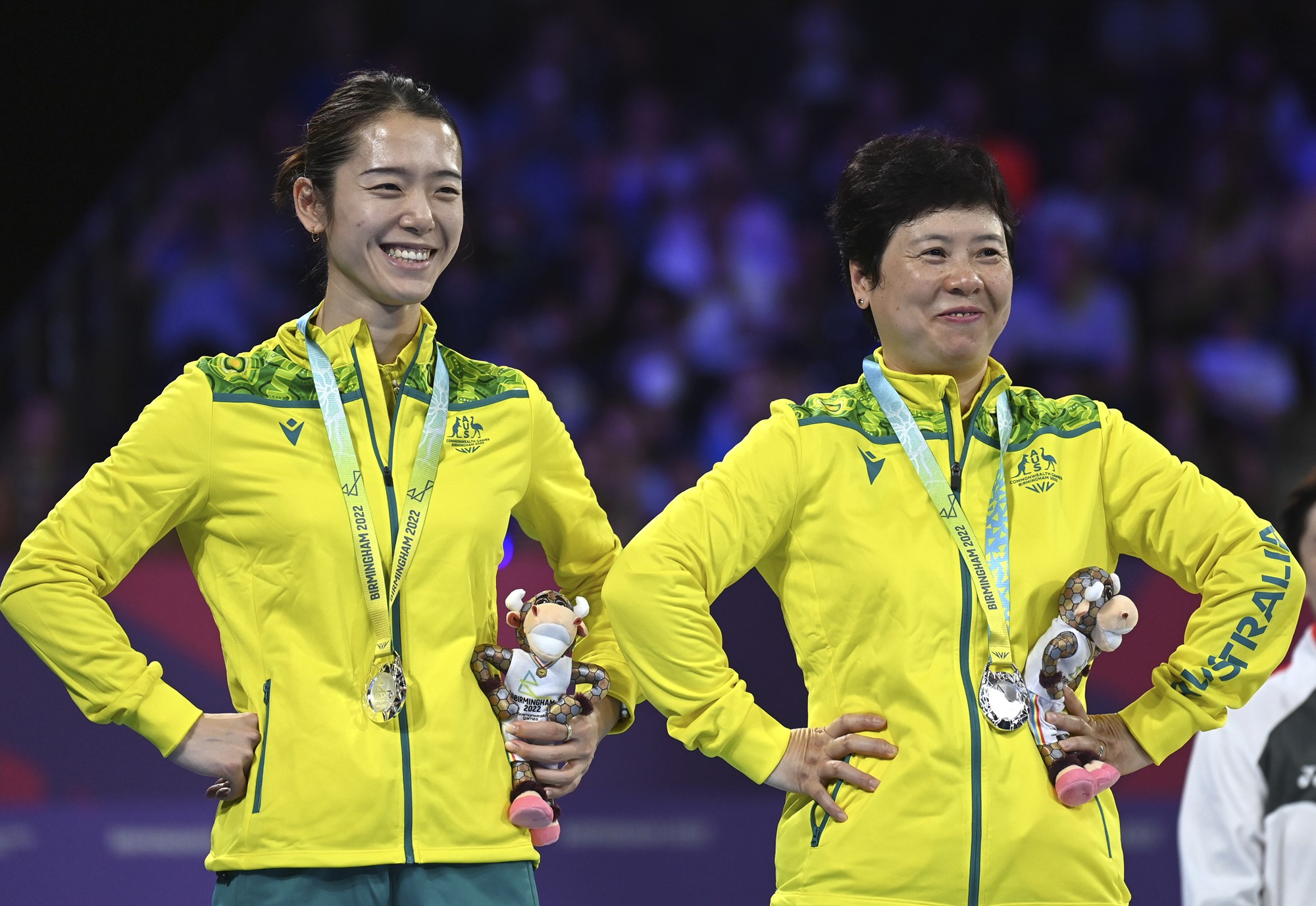 Table tennis players Jian Fang Lay and Minhyung Jee smile with hands on hips on the podium at the Commonwealth Games.
