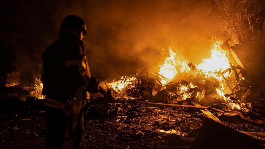 A firefighter working in the dark on a large blaze of metal