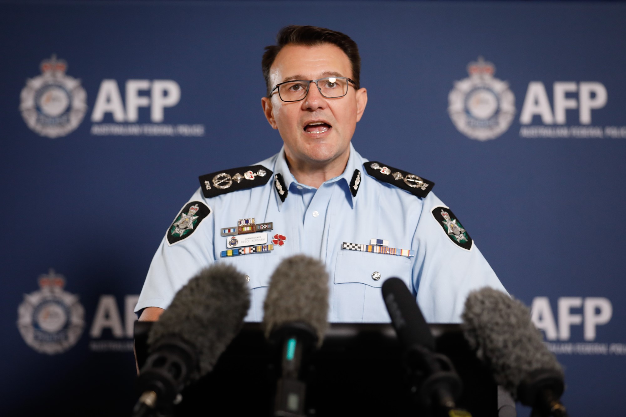 A man in an AFP uniform and glasses stands behind a podium addressing the media.